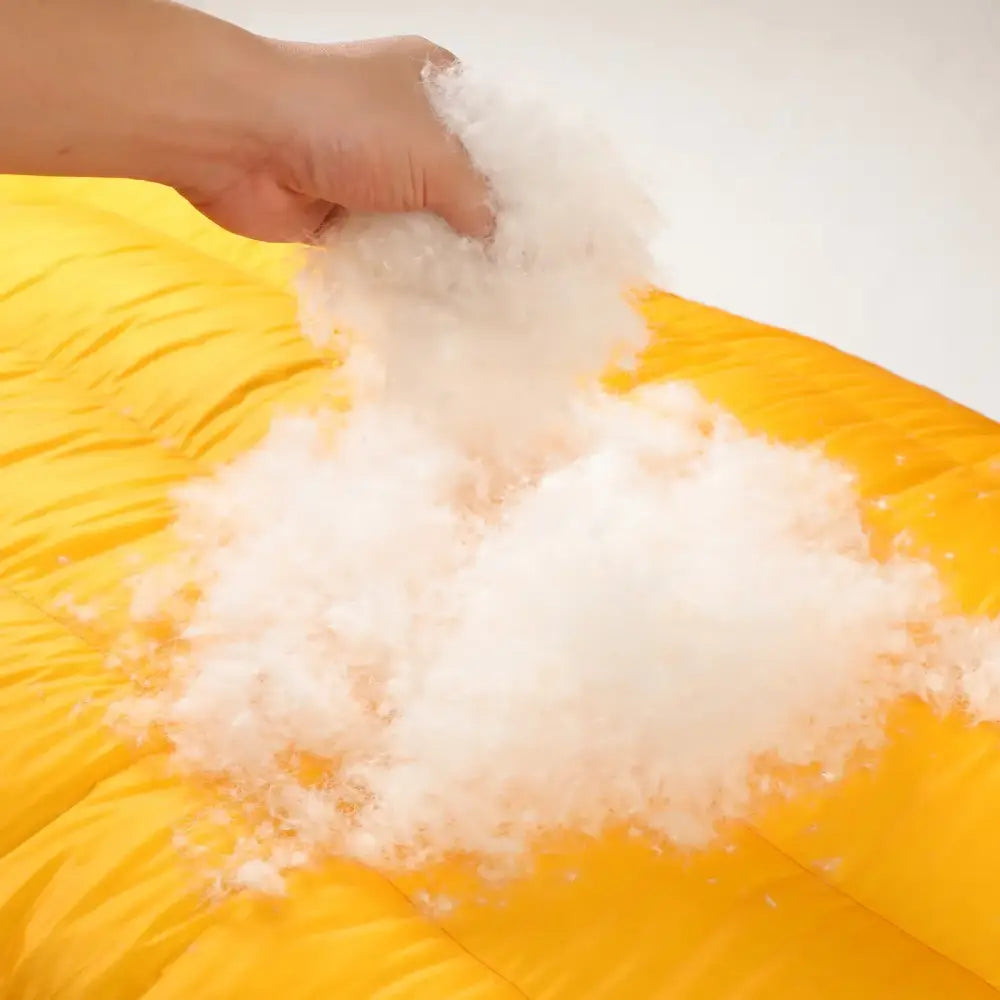 Fluffy white cotton or polyester fiberfill being placed on a yellow surface.