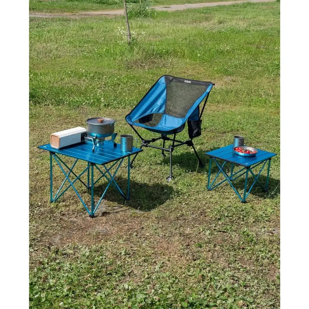 Portable camping chair with matching blue folding tables set up on grass.