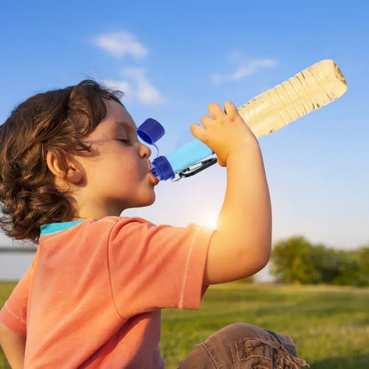 Child drinking from a large water bottle outdoors.