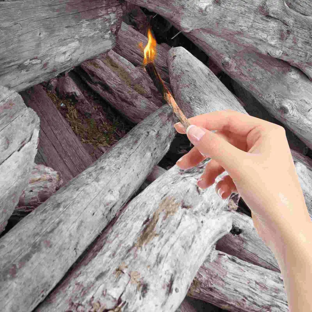 Lit match held by a hand over weathered wooden planks.