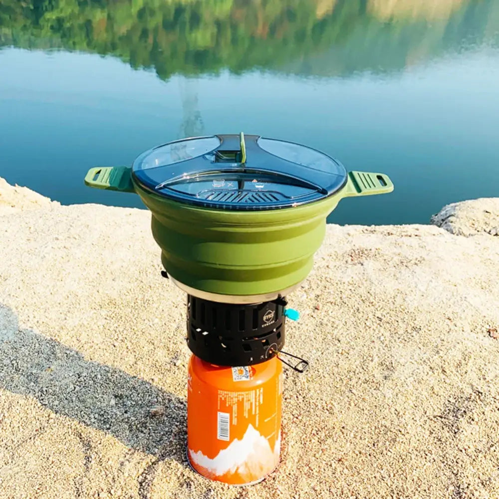 Portable camping stove with a green collapsible pot on top of an orange fuel canister.