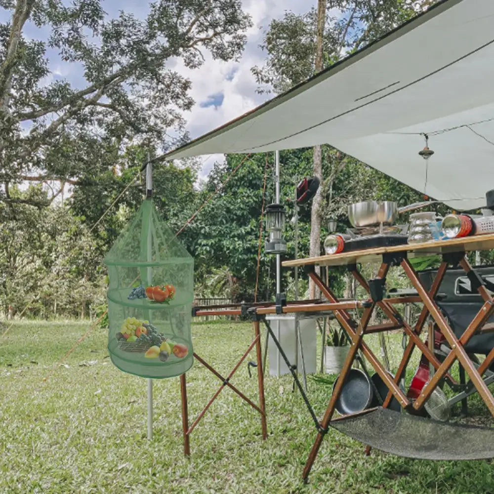 Outdoor camping kitchen setup with folding tables and cooking equipment under a canopy.