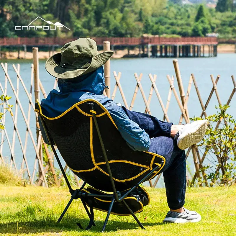 Portable camping chair with a person seated in it, wearing a hat and blue jacket.