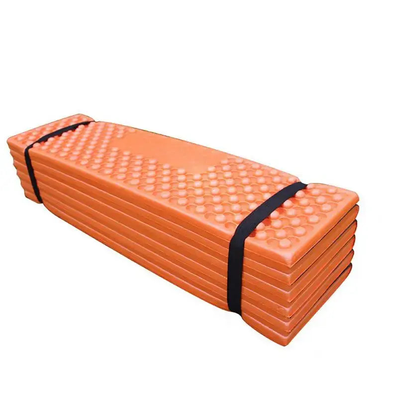 Folded orange foam camping mat with textured surface and black straps.