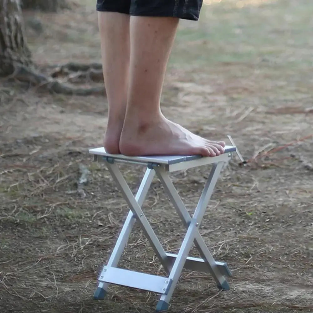 Folding metal stool with bare feet standing on it.