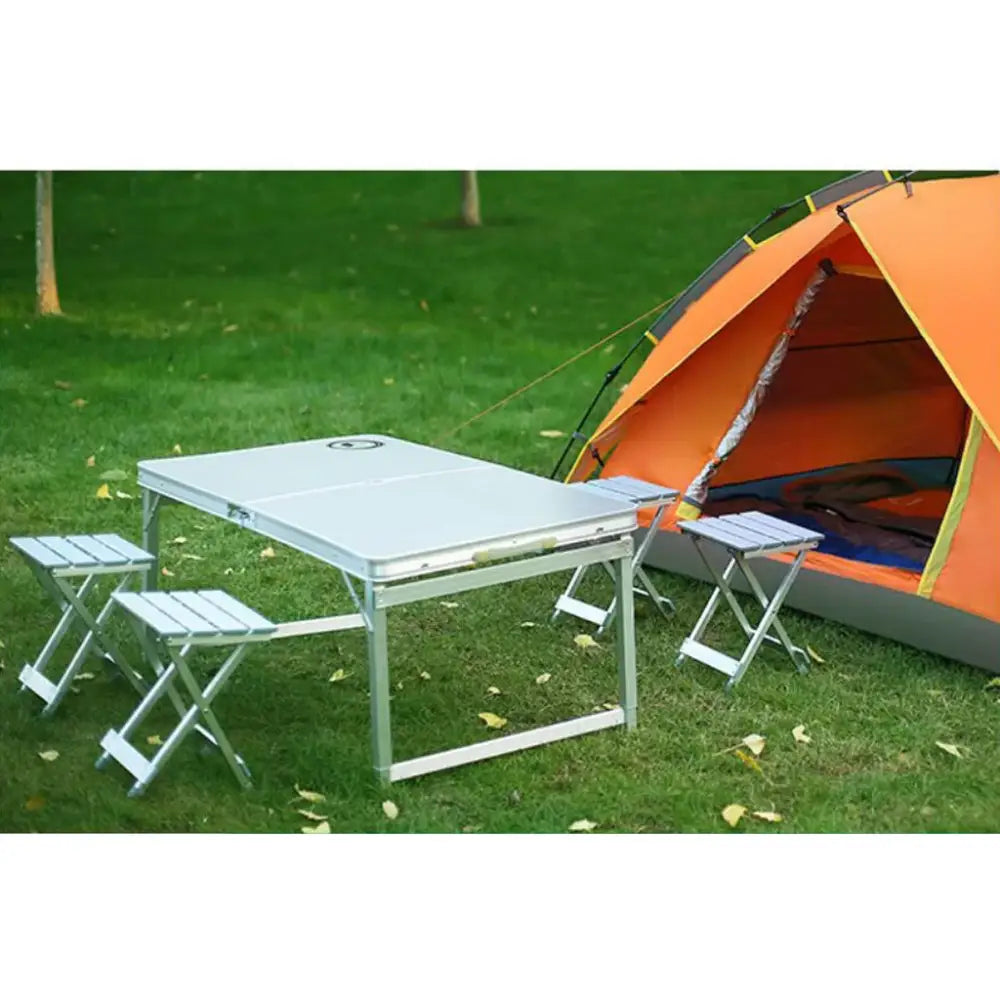 Portable folding camping table with attached stools set up near an orange tent on grass.