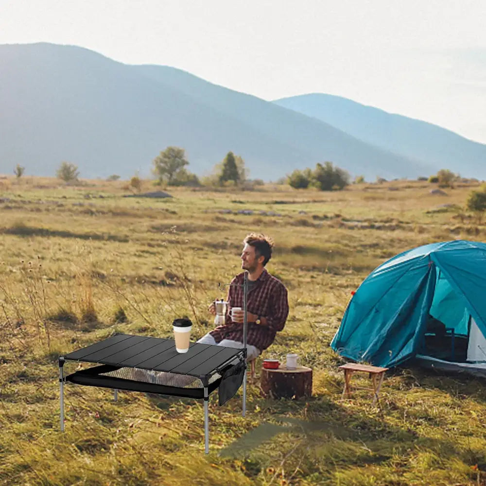 Camper sitting at a portable table next to a tent in a grassy field.