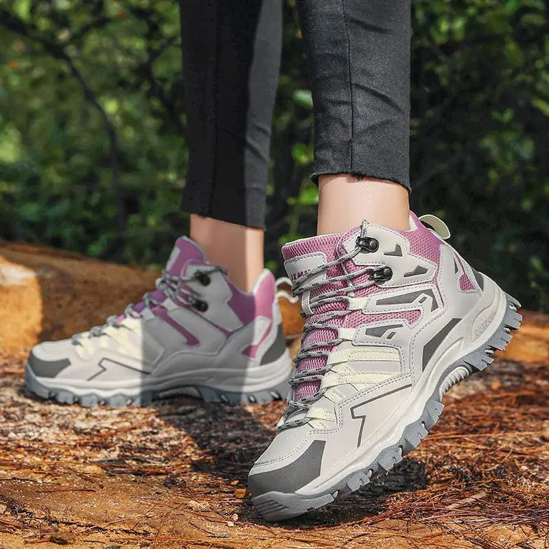 Pair of gray and pink hiking boots with rugged soles on a forest trail.