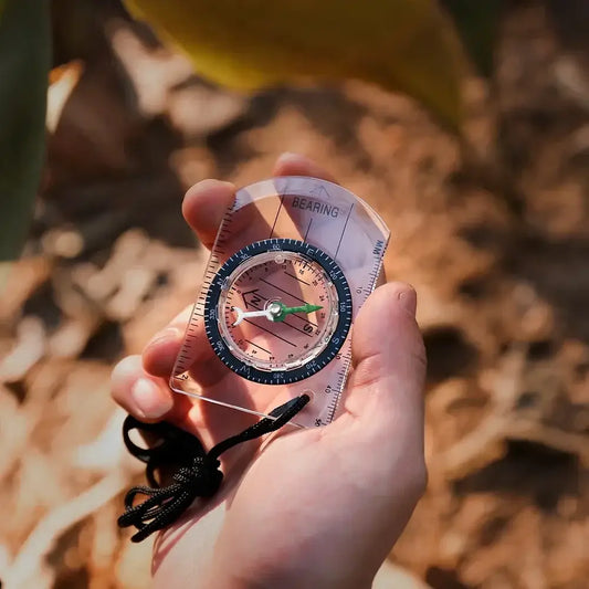 Handheld compass with a transparent base plate held over autumn leaves.