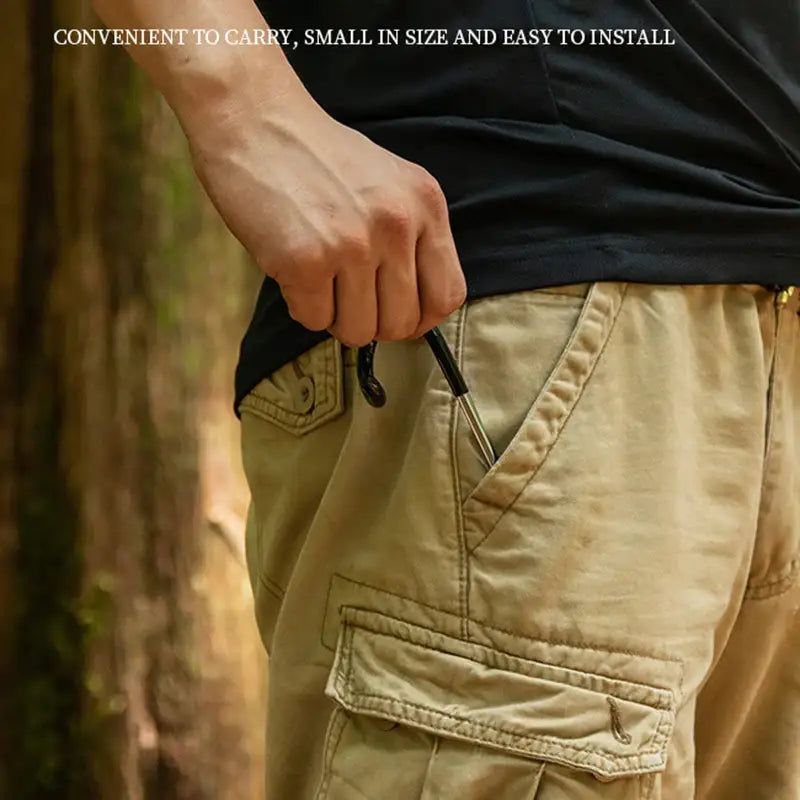 Hand holding a small black object, possibly a compact tool or device, near the pocket of khaki cargo pants.