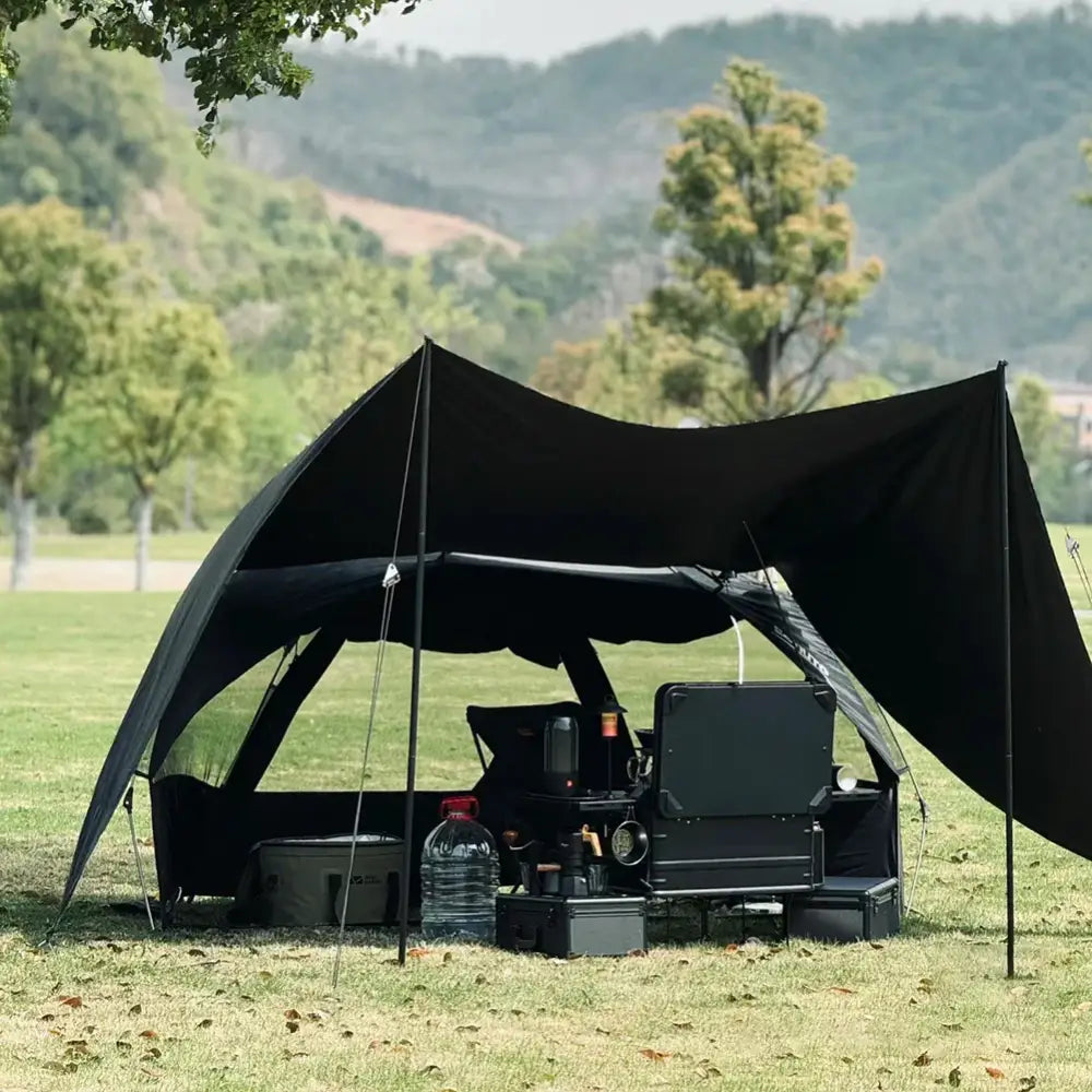 Black canopy tent set up over camping gear in a grassy area.