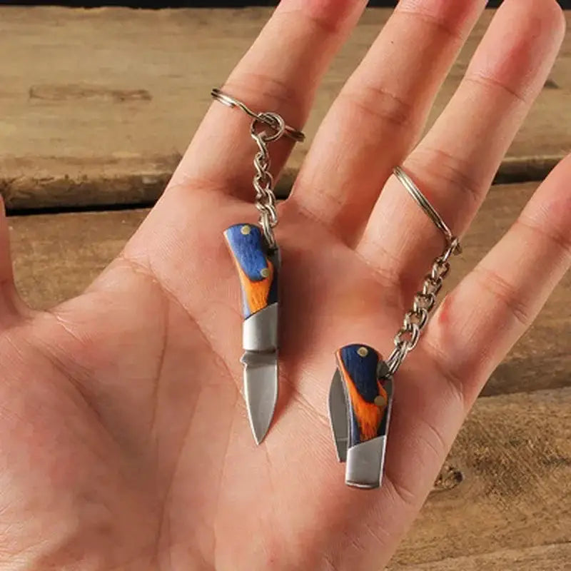 Miniature knife charm with a blue and orange handle attached to a keychain.