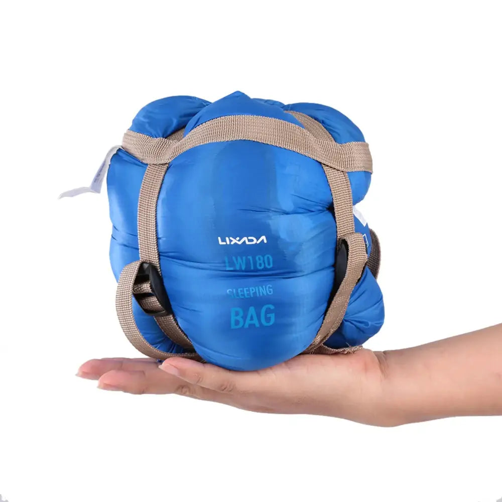 Bright blue compact sleeping bag with tan straps held in a person’s palm.