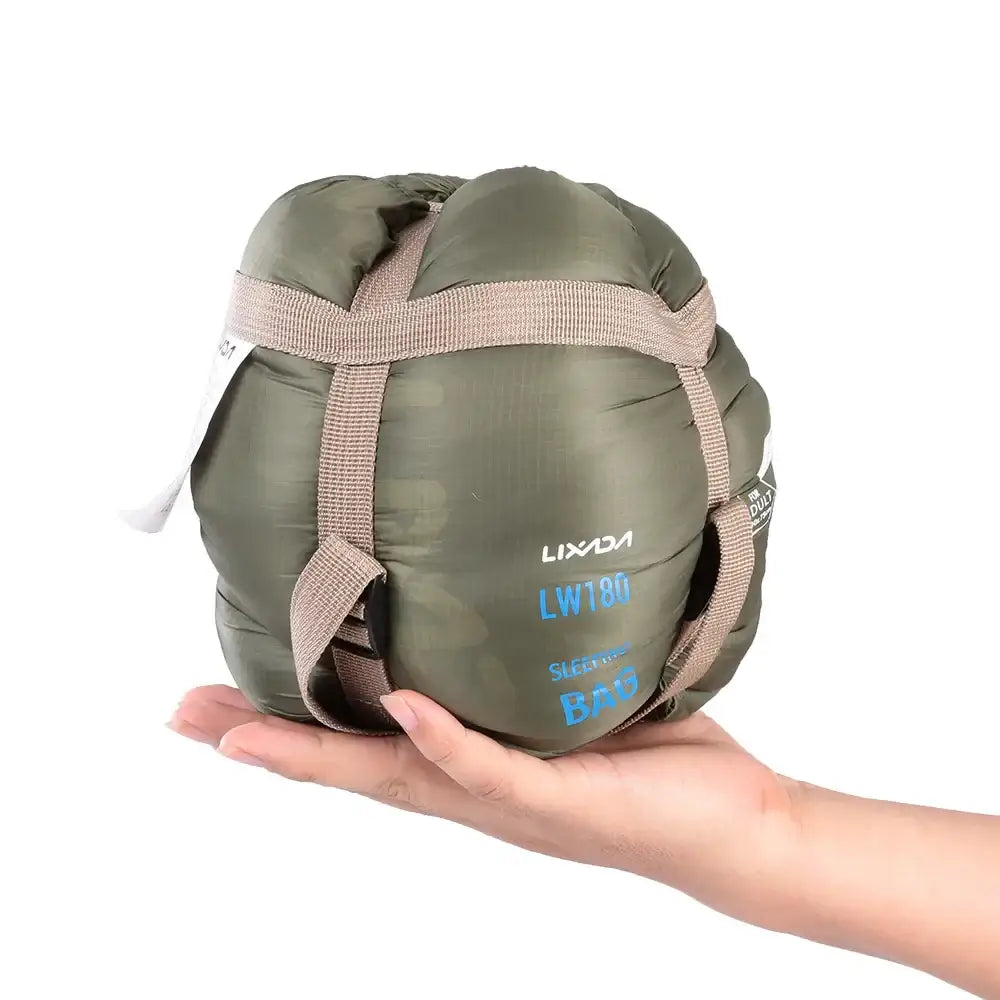 Compact olive green sleeping bag held in a person’s hand.