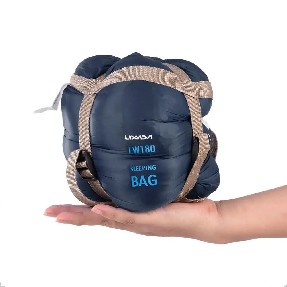 Compact navy blue sleeping bag with tan straps held in a hand.