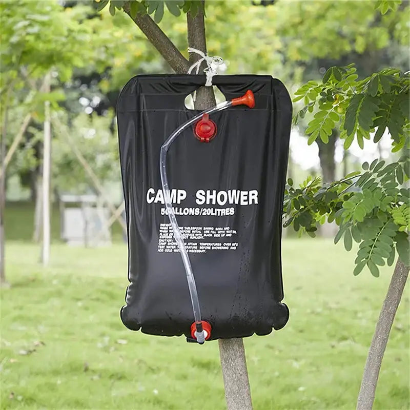 Portable camping shower bag hanging from a tree branch.