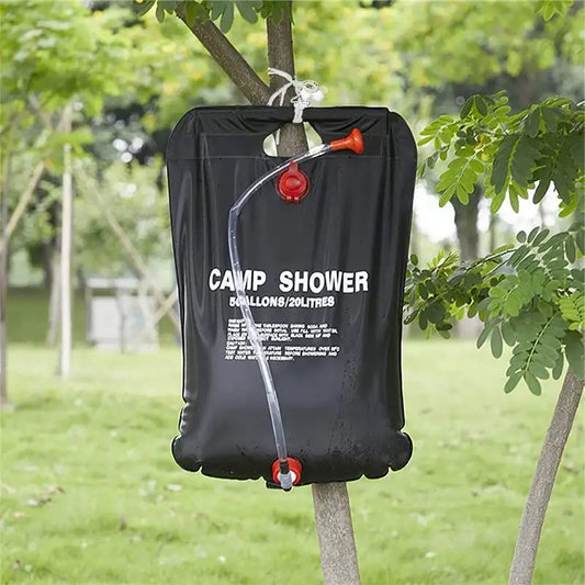 Portable camping shower bag hanging from a tree branch.