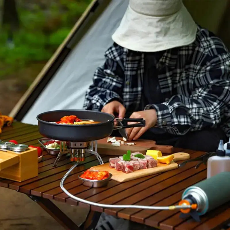 Portable camping stove with a pan and various food ingredients on a wooden table.