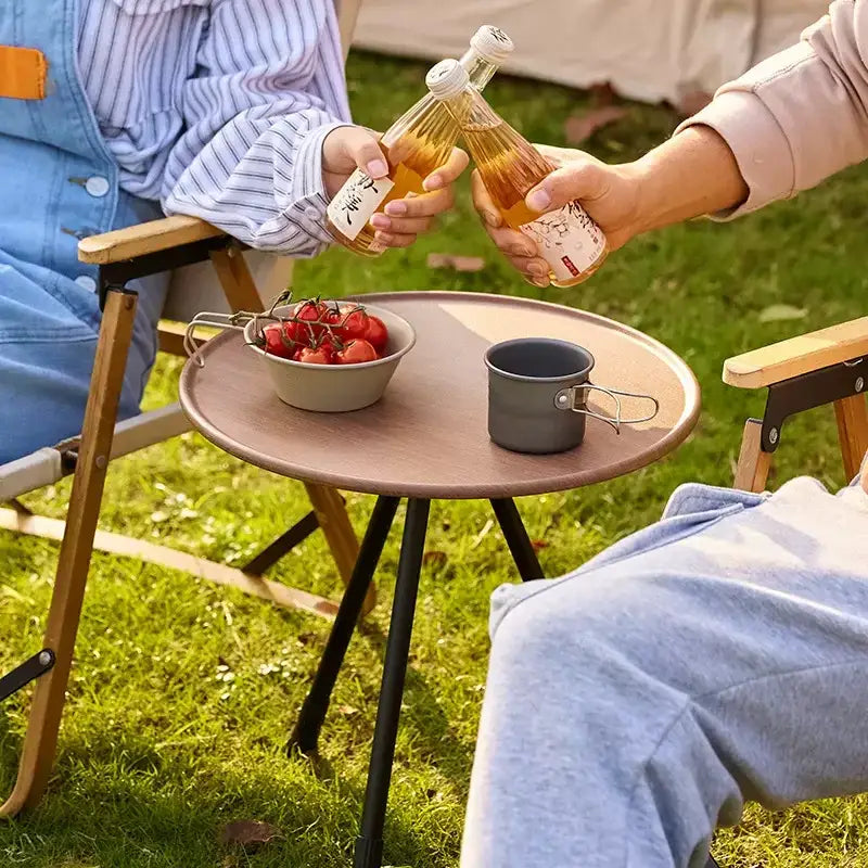 Round wooden side table with metal legs holding food and drinks for an outdoor gathering.