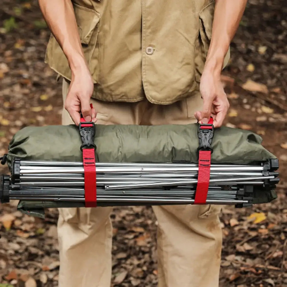 Folded tripod secured with red straps, held by hands in khaki clothing.