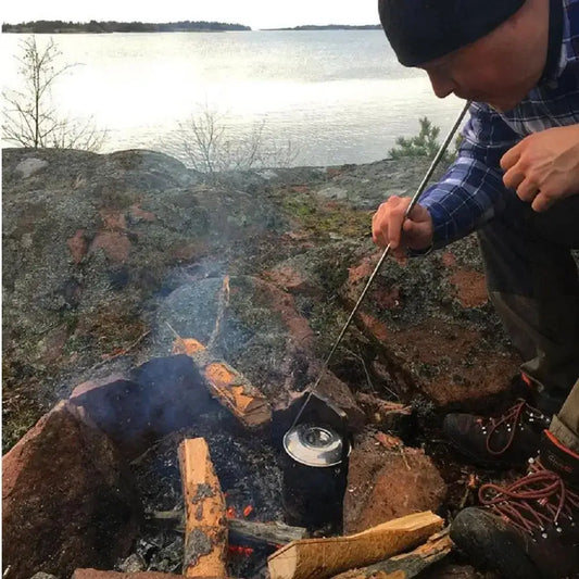 Campfire with a pot and person roasting food on a stick.