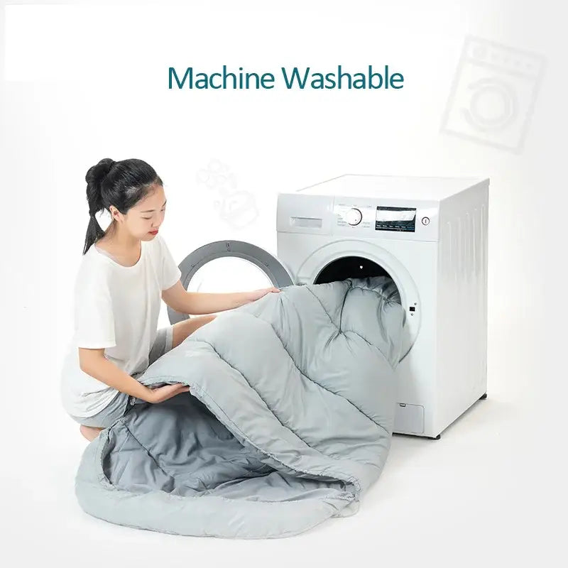 A gray comforter or duvet being loaded into a washing machine.