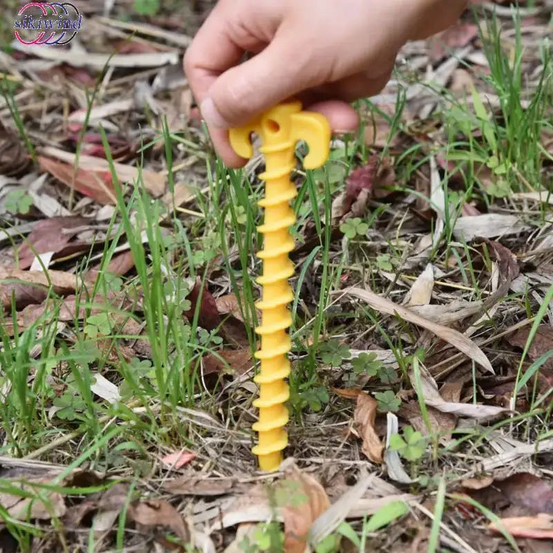 Yellow plastic spiral tent stake or peg being inserted into grassy ground.