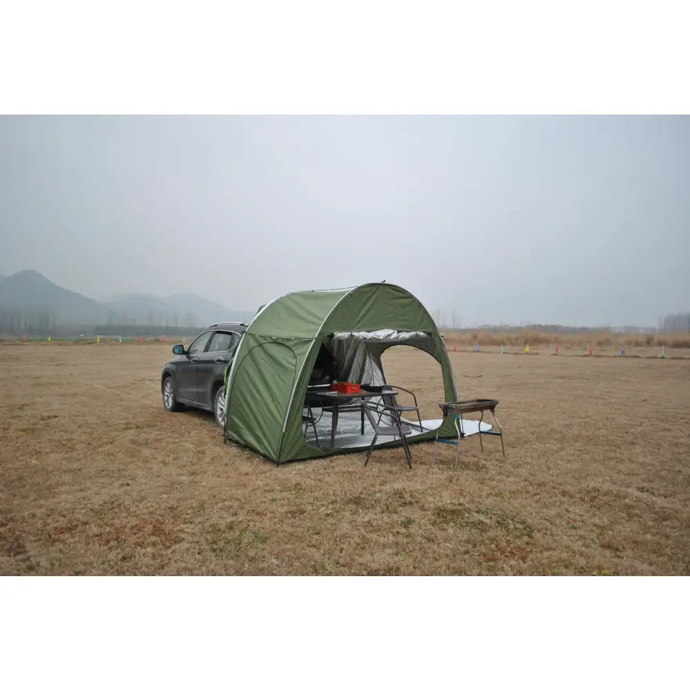 Green tent-like structure attached to the rear of a vehicle for camping.