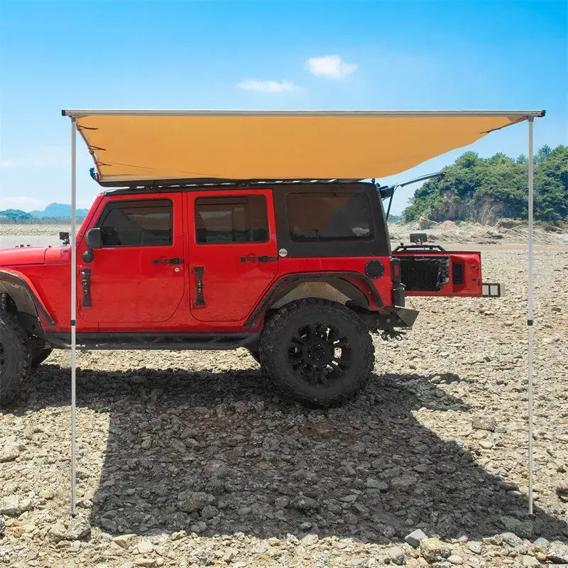 Red Jeep Wrangler with an attached awning parked on rocky terrain.