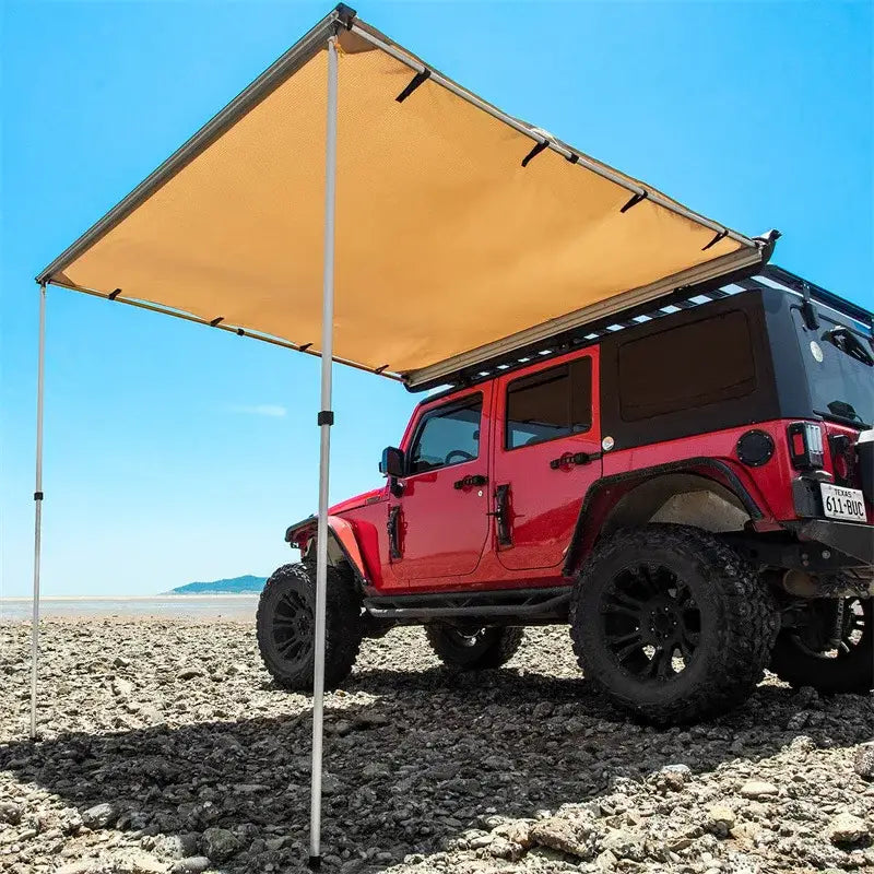 Red Jeep Wrangler with an attached tan awning on a beach.