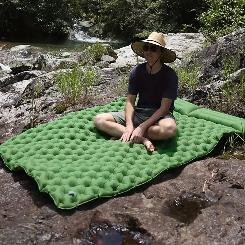 Inflatable green camping mat on rocky terrain near a stream.