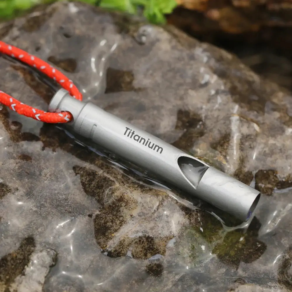 Titanium whistle with a red cord attached.