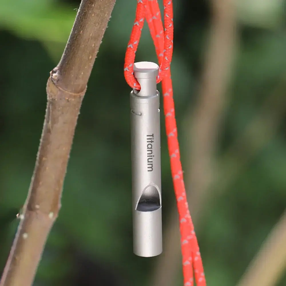 Metallic titanium whistle suspended by a red cord.