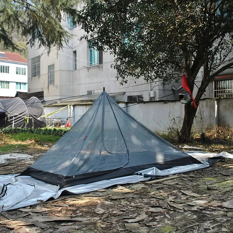 Pyramid-shaped camping tent set up on uneven ground.