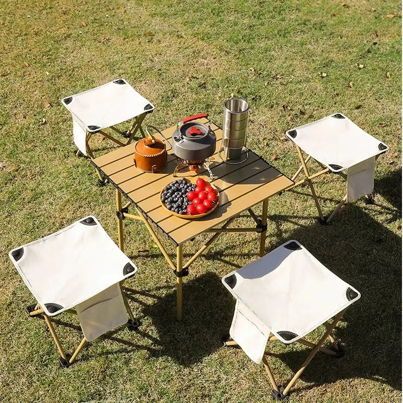 Portable camping table with folding chairs set up on grass.