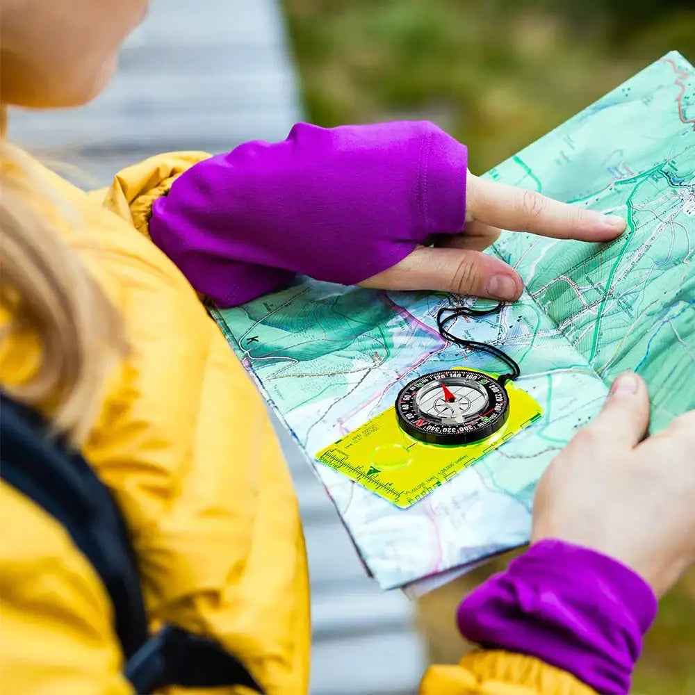 Map with a compass being held by hands wearing purple gloves.